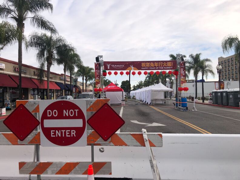 Blockades and a Do Not enter sign block a road where tents sit empty. A decorative sign stretches across the road with red lanterns hanging from it.