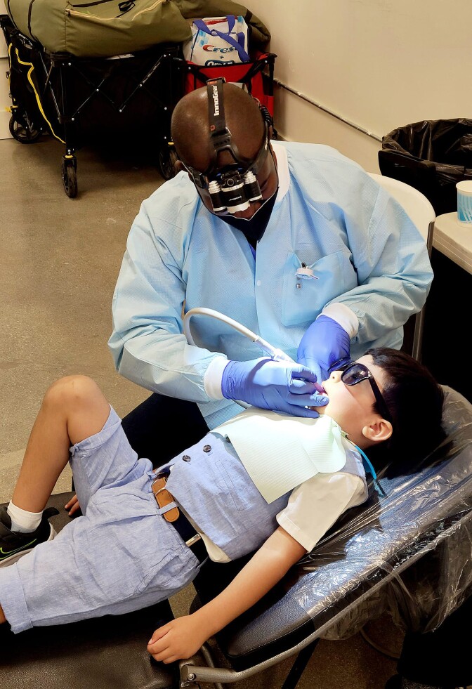 A Black dental hygienist examines a Native American child at a children's health event.