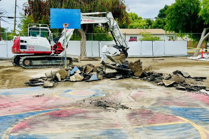A backhoe next to a school yard, broken asphalt next to it.