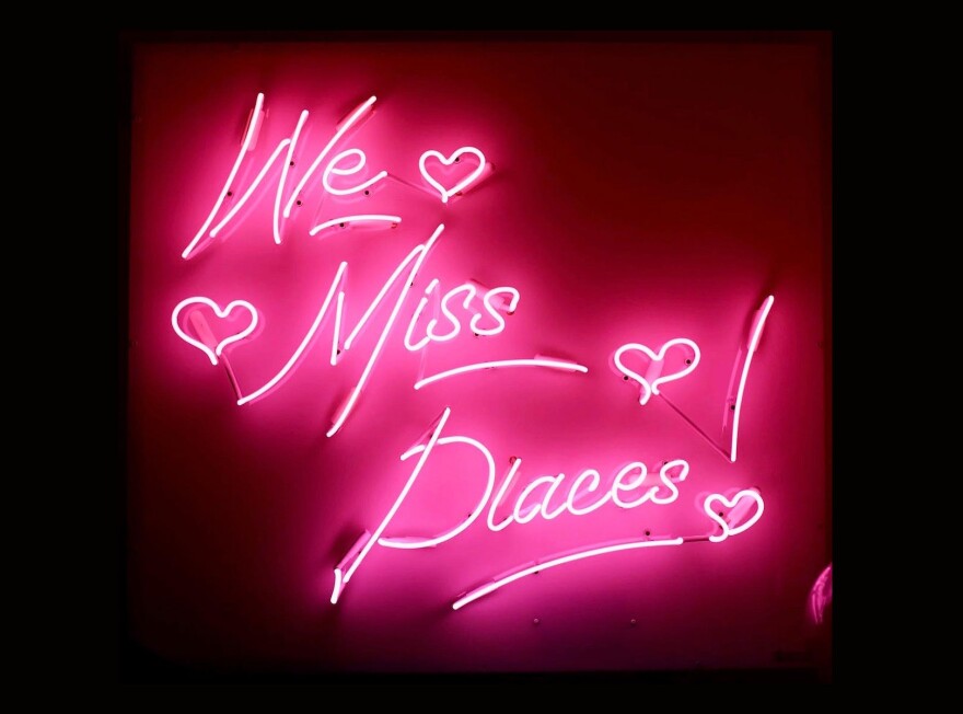 A pink neon sign reads "We miss places!"