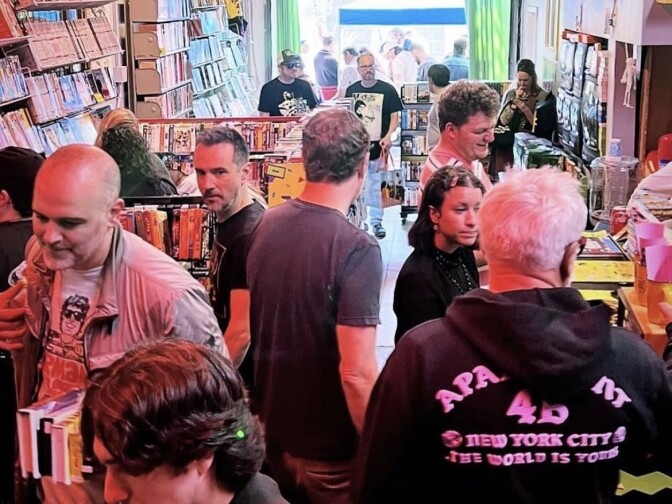 Several people are seen walking through Whammy Analog Media looking for VHS Tapes to buy. A man on the left side of the picture is seen with five tapes in a single hand.