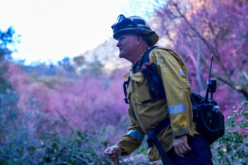 A firefighter standing in front of vegetation coated in fire retardant.