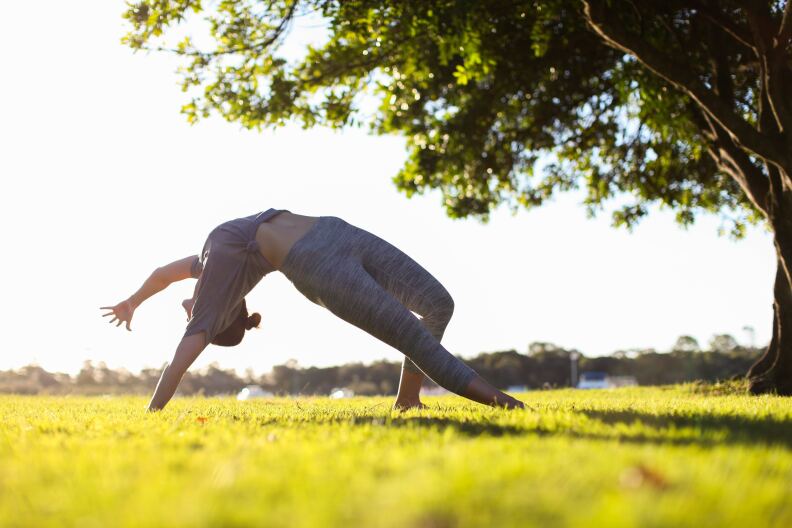A person does a yoga pose on a large outdoor grassy area.