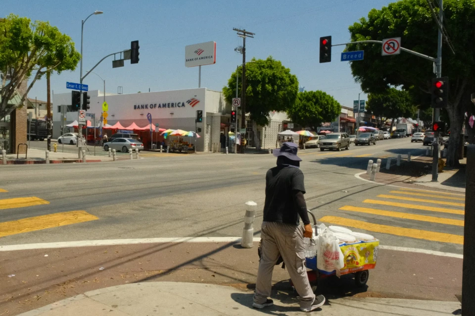 A street vendor pushes a cart past a Bank of America at the intersection of Cesar E. Chavez Avenue and Breed Street.