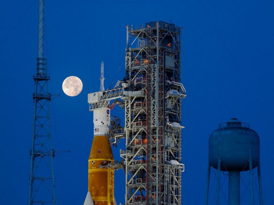 A rocket sits in the launch station with a big round moon in the background