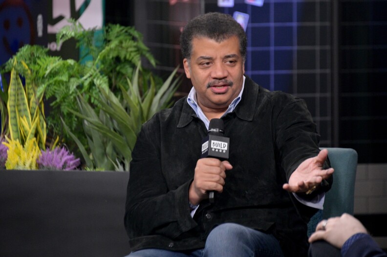 Neil deGrasse Tyson sitting on a couch with a mic in hand.