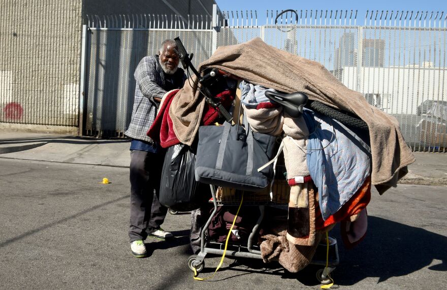 A homeless man pushes his cart of belongings along a street in Los Angeles, California on February 9, 2016.