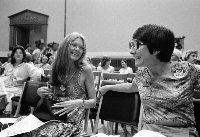 A black and white photo of two women sitting next to each other, chatting and smiling.