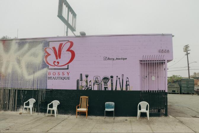 Five chairs are place along the wall of a building painted pink and black. On the building a butterfly is painted in red above the words "bossy boutique"