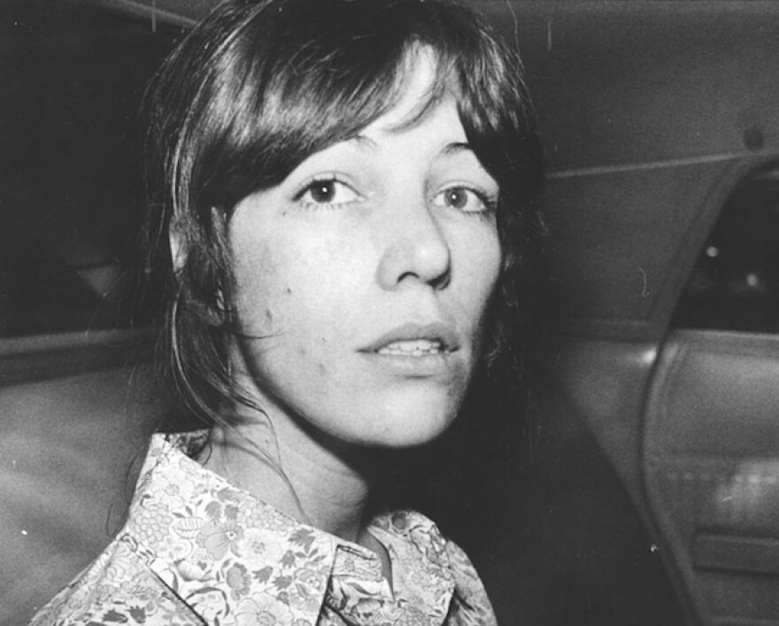 A woman with light-tone skin has large eyes and dark hair cut in a shag cut. She's in the back of a car.