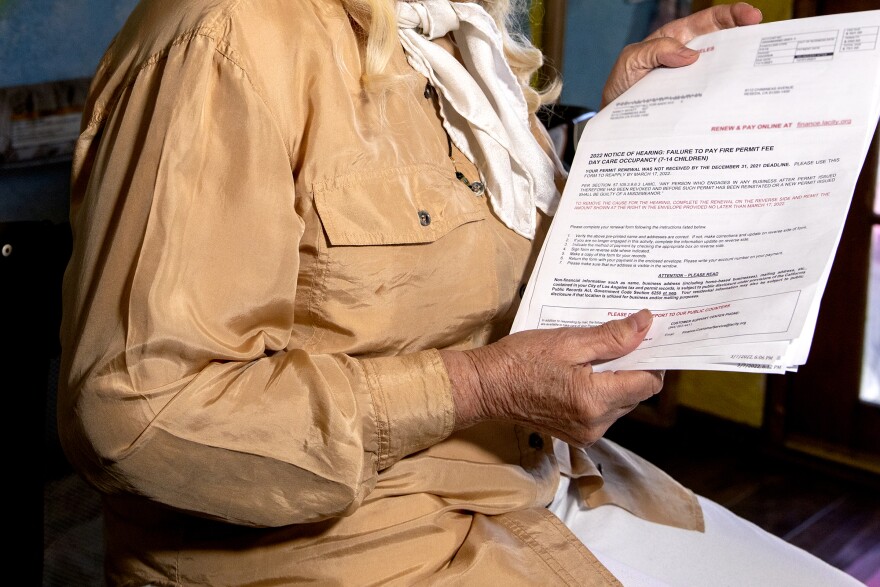 A woman in a beige shirt, with a white scarf and white hair holds a notice saying she failed to pay a fire permit.