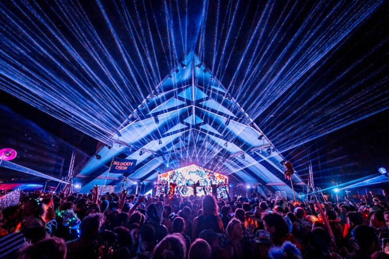 A pyramid-like structure at night with lights shooting out toward the crowd.