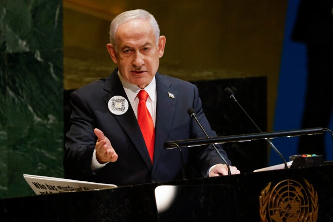Benjamin Netanyahu, in a suit and tie, gestures at a lectern.