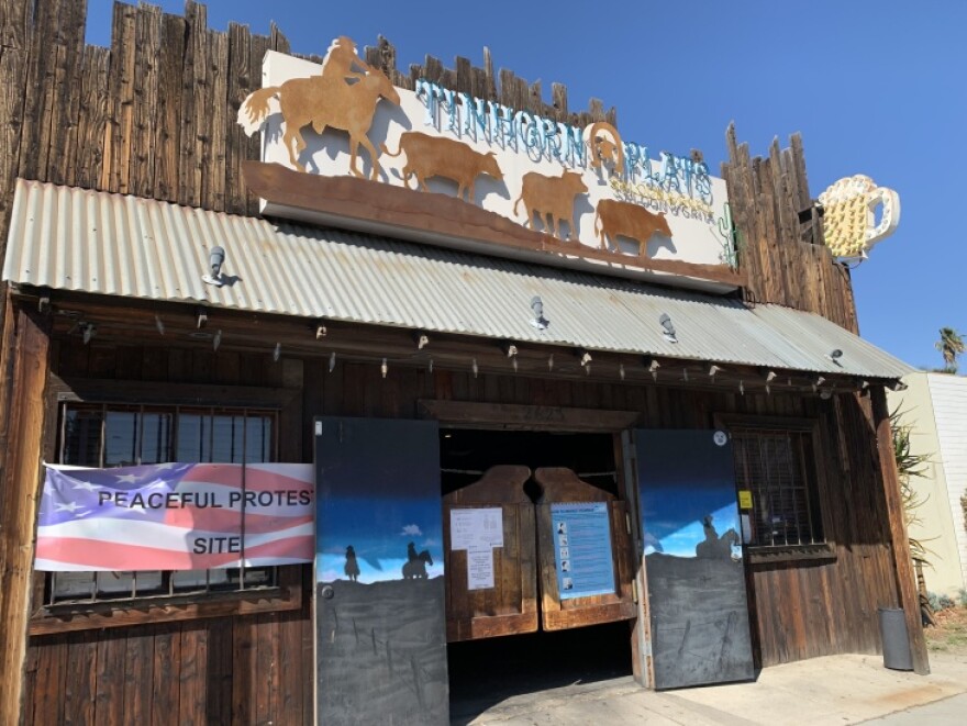 A side angle of the exterior of Tinhorn Flats saloon with wooden swinging doors and a tin roof awning