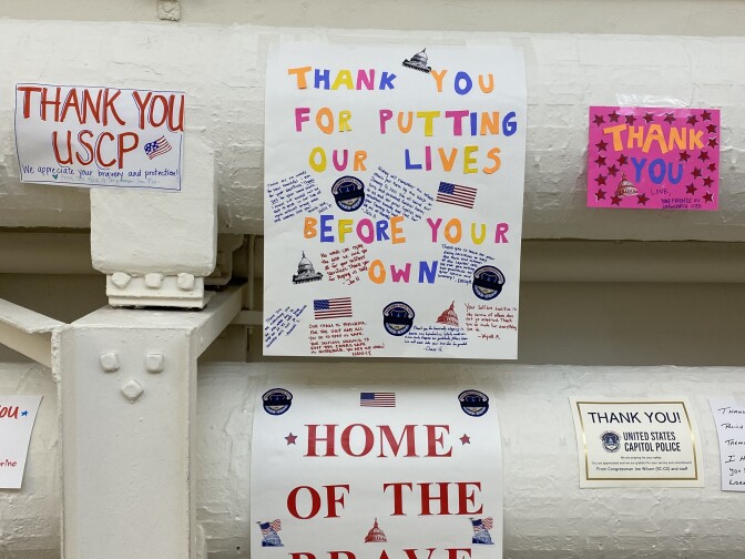 A series of handmade signs are affixed to large white horizontal tubes in an interior space. The signs read "Thank you USCP" "Home of the Brave" and "Thank you for putting our lives before your own."