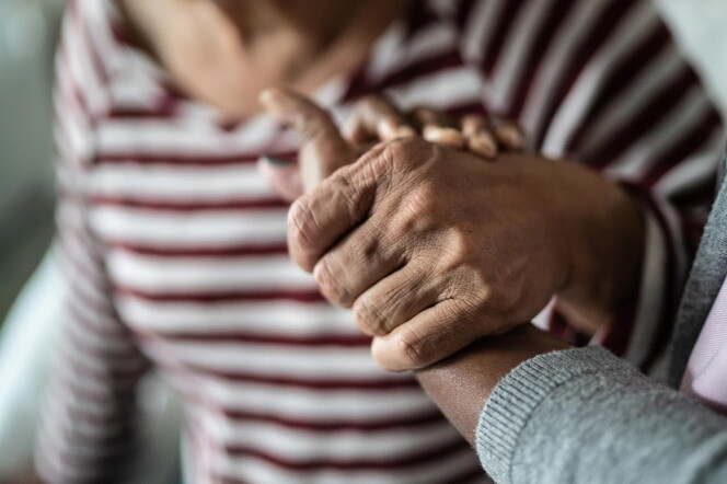 Two hands holding each other are shown in close-up. They appear to be women and their skin is medium-brown. 