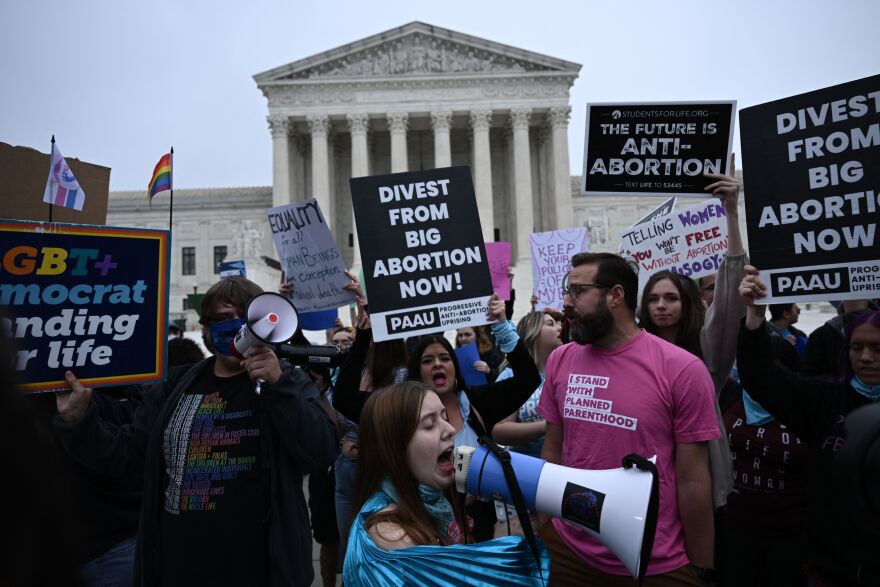 A crowd of people hold anti- and pro-abortion signs outside the U.S. Supreme Court building.