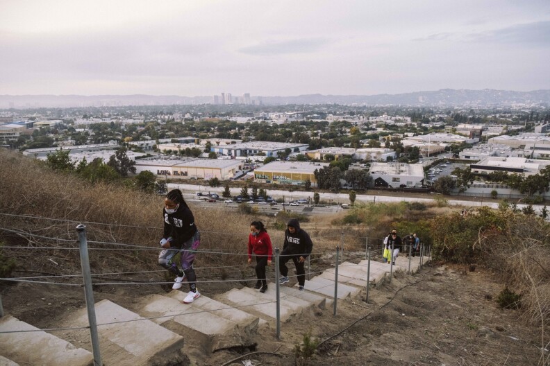 Masked hikers climb up the Baldwin Hills Scenic overlook's stairs as the sun sets.