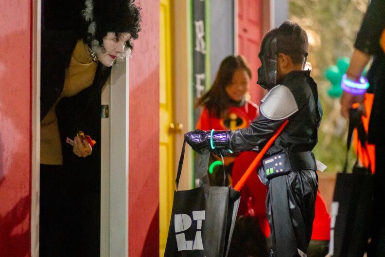 A child dressed as Darth Vader holds open his DTLA-branded Halloween bag to get candy from an adult dressed in white makeup and a Bride of Frankenstein wig.