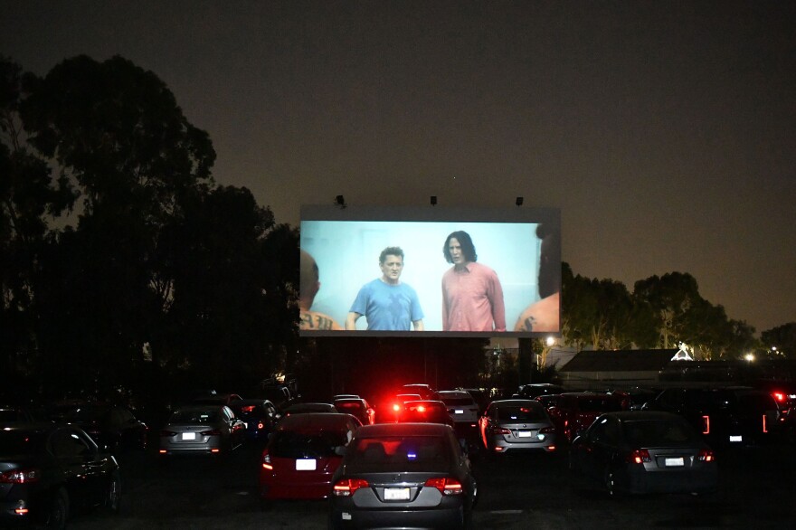 A film is projected onto large outdoor screen with rows of cars facing the action.