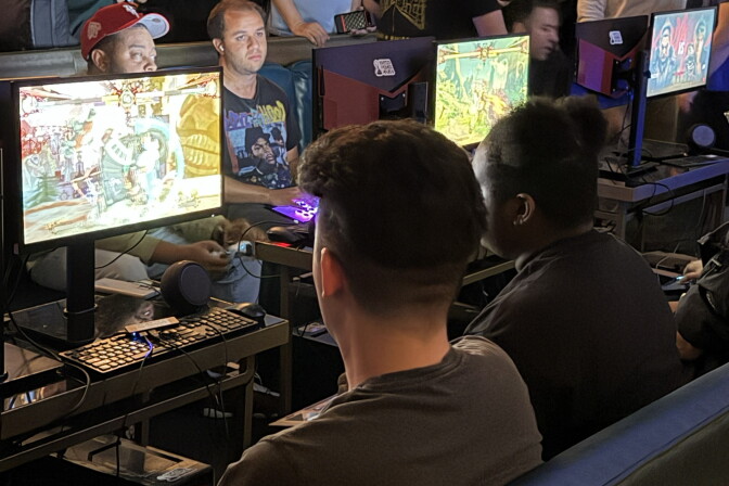 A group of people sitting in front of monitors and playing Street Fighter 6.