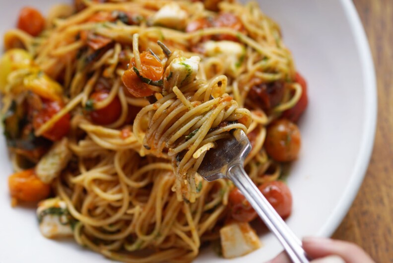 a bowl of Spaghettini Alla Checca with cherry tomatoes. Spaghetti is twisted around a fork.