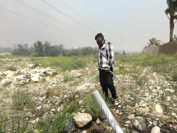 Ernesto Dominguez hosing down brush near his cousin's house as the Etiwanda Fire nears Banyan Avenue on Wednesday, April 30, 2014.