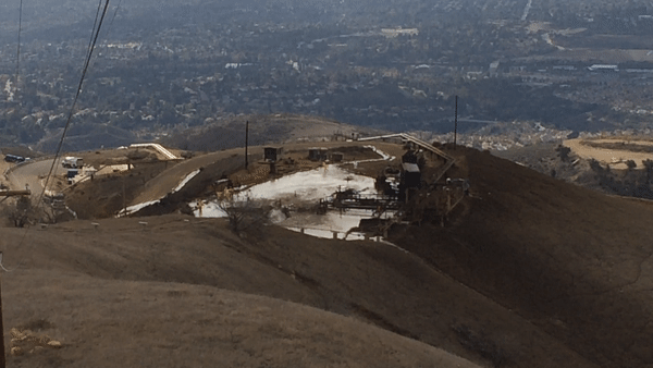 A gif of a methane leak coming from a well on a brown hill overlooking an urban area.
