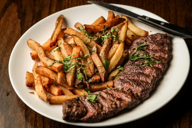 A sliced steak sitting next to a batch of french fries on a plate with a knife.