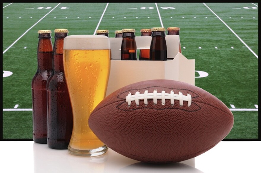 A football with beer glasses at the foreground, and in the back there's a football field.