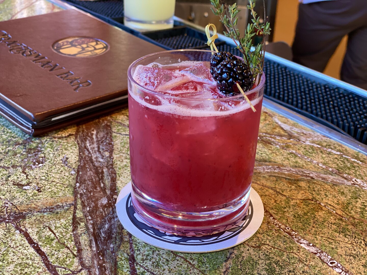 a glass of red liquid topped with a couple blackberries speared with a toothpick