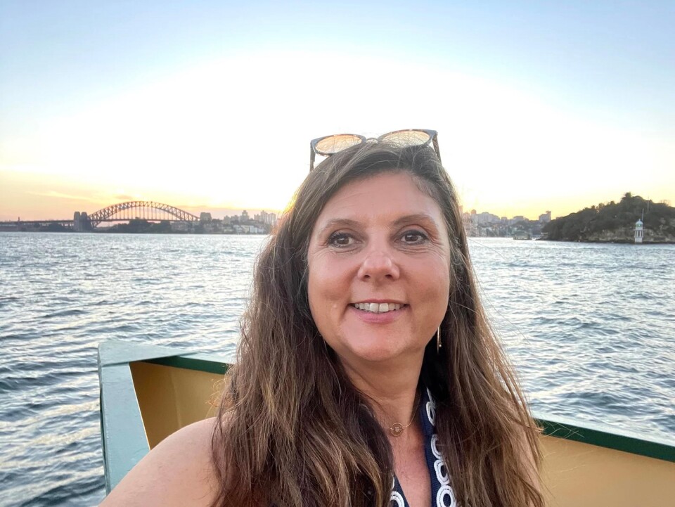 A white woman takes a selfie while in a boat, on ocean water. She has long, dark hair with some lighter highlights and is wearing sunglasses on top of her head. 