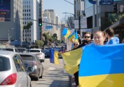Several people stand on the side of a busy urban street holding Ukrainian flags.