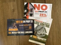 Three colorful mailers on a hardwood floor. One has a large picture of a house wrapped in chains with the words, "Are you ready to lose control of your property?" Another shows a somber woman with the word "Vote no on Prop 33." Another has the cracked facade of a building with the words "No on Prop 33." 