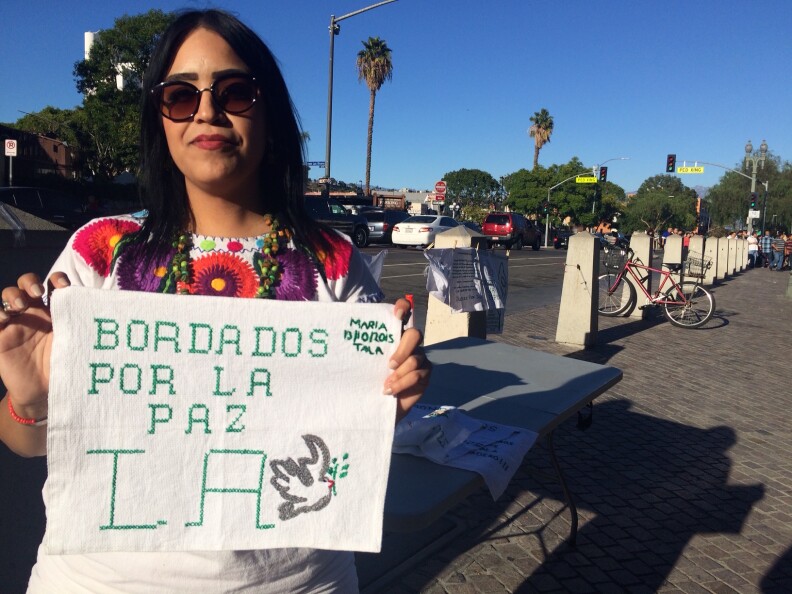 Nansi Cisneros holds a piece of embroidery that she brought back from Jalisco, Mexico, part of a project to honor the missing in Mexico. The piece reads, 'Embroidery for Peace, Los Angeles,' in Spanish.