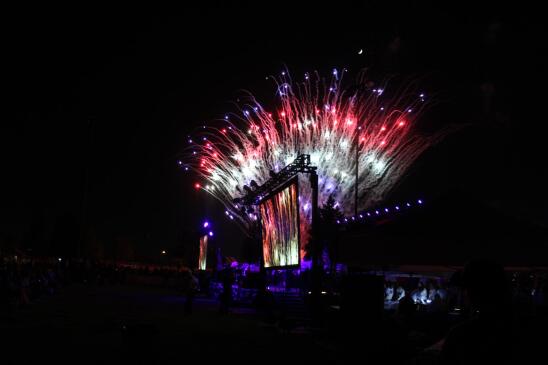 Red, white and blue fireworks shoot up into the inky black night sky from a stage.