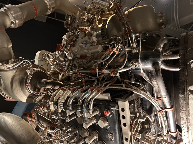 A close-up of intricate silver metal pieces, wiring and welding. It's part of the main engine of a space shuttle.