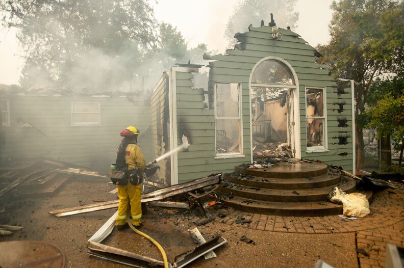 A firefighter hoses down the shell of a burned home.