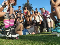 A diverse group of people in roller skates are stretched out on a lawn with palm trees behind them