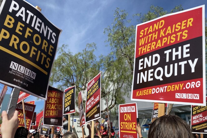 Picketers hold high red, yellow and black strike signs. They read: "Stand with Kaiser therapists" and "Patients before profits" 