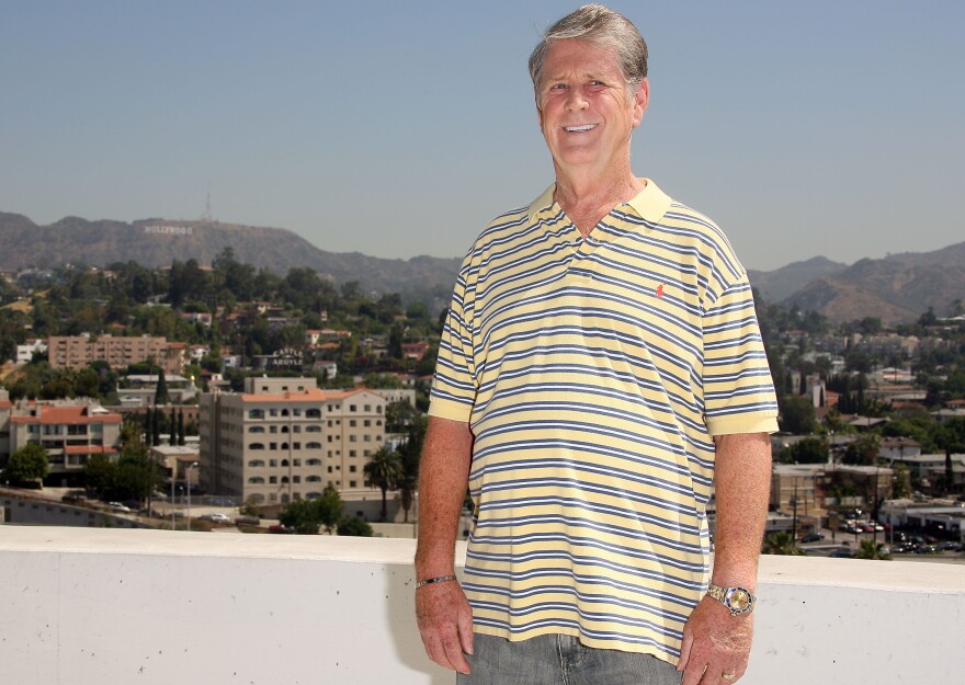 A white man in a striped polo shirt poses on a rooftop with a view toward the Hollywood sign.