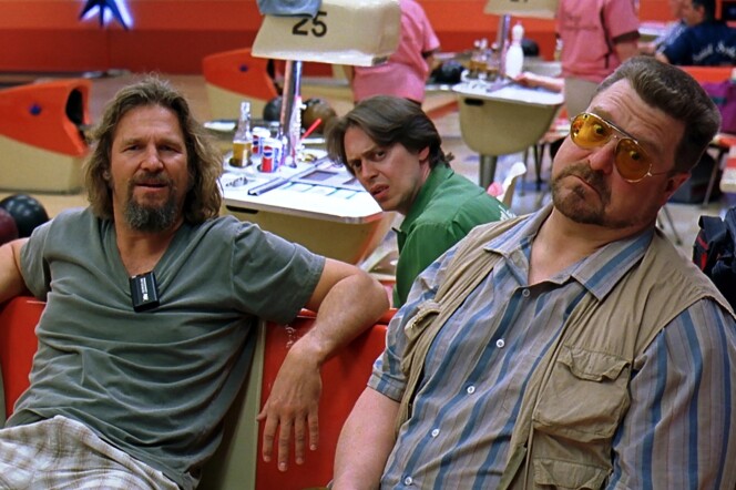 Three men sit in a bowling alley, looking toward camera in a still from the movie 'The Big Lebowski.' 