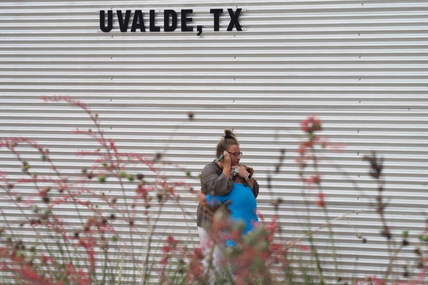 Two people embrace in front of a corrugated metal wall with the sign Uvalde, TX