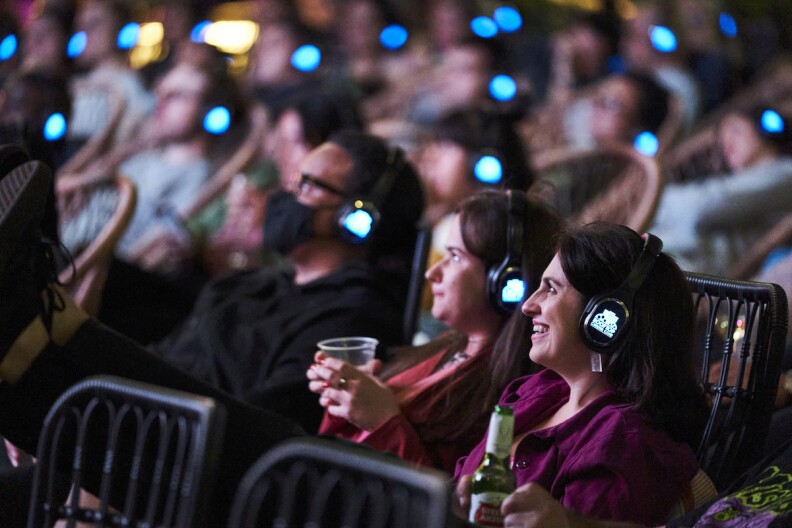 People sitting watching an outdoor movie with wireless headphones. Some have drinks in their hands.