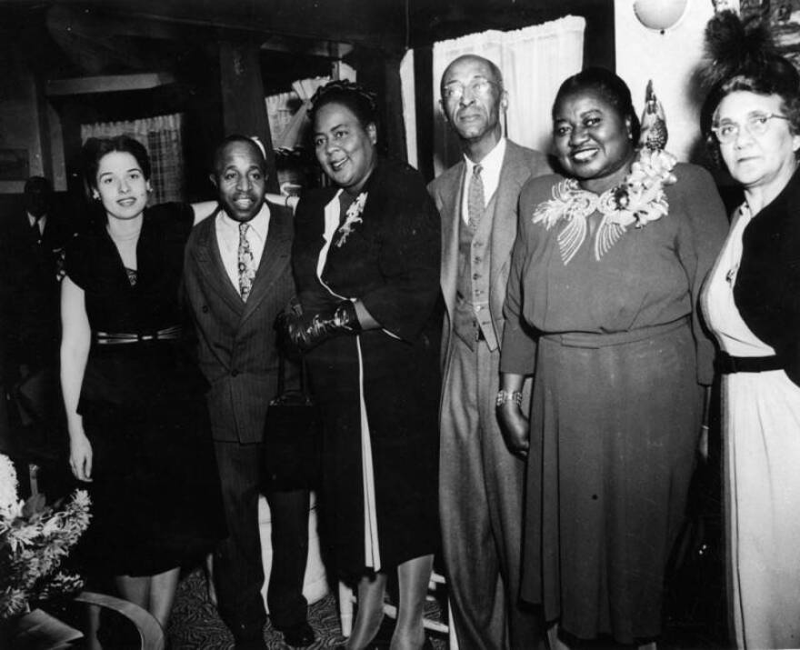 Black and white photo, circa 1948, of two men and four women, most of whom are Black, and dressed up in nice clothes as if at a party.