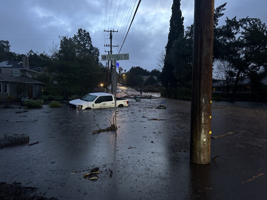 A white truck is submerged in solid mud near a street sign in a neighborhood.