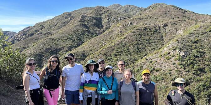 A group of ten people posing for a photo in front of hills and a blue sky during a hike. 