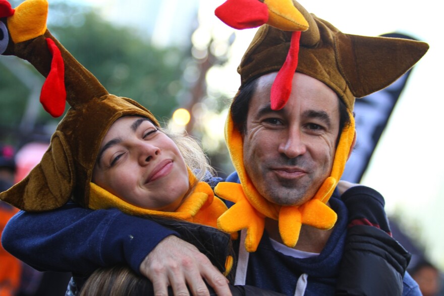 A couple wearing cloth turkey hats both smile for the camera while embracing.