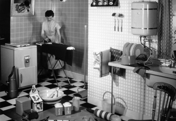 A woman ironing in the corner of her tidy and well-equipped kitchen.   (Photo by Hulton Archive/Getty Images)