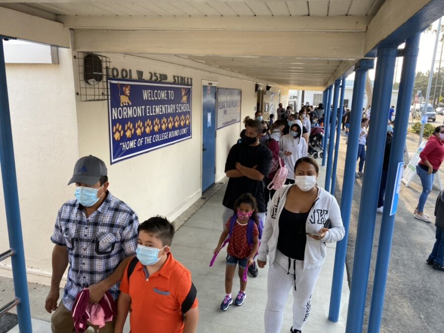 Parents and students in mask line up outside a school.